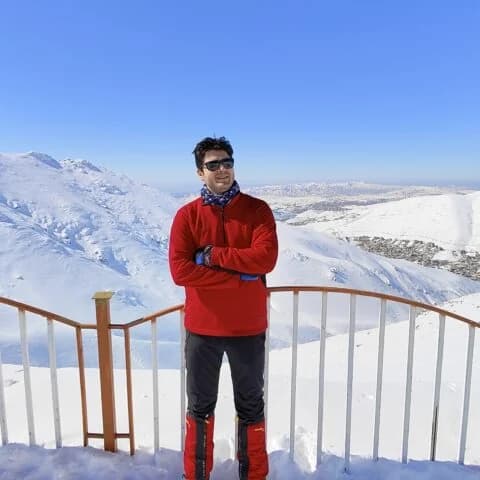 Arian Azmoudeh on a snow-covered mountain viewpoint, arms crossed